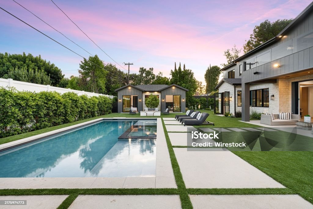 Modern backyard with a swimming pool, lounge chairs, and a guest house under a beautiful sunset sky.
